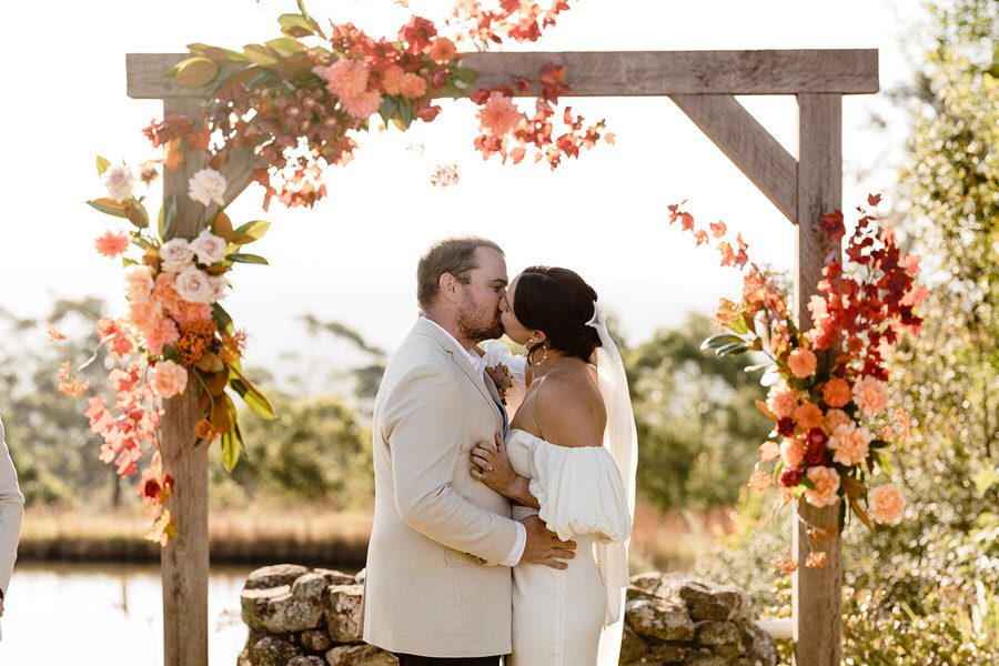 First kiss at the Barn on the ridge. Couple standing infront of wedding arbour decorated in autumn style florals 