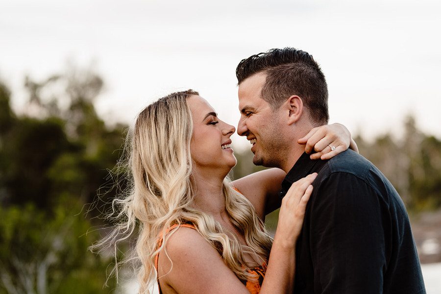 blonde lady looking into a mans eyes and touching noses with the biggest smiles on their faces in their engagement shoot
