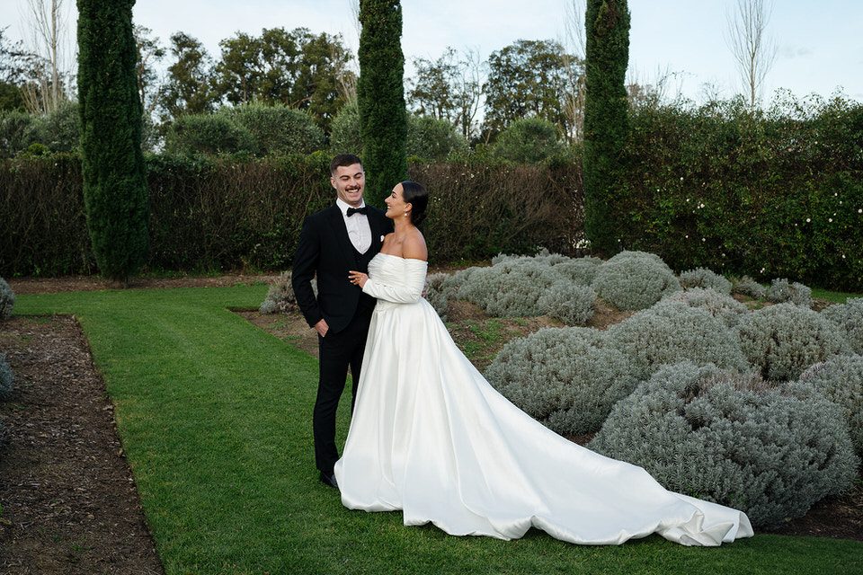 Bride and groom share a quiet moment in the lavender garden at The Merribee, framed by tall cypress trees and silver foliage.