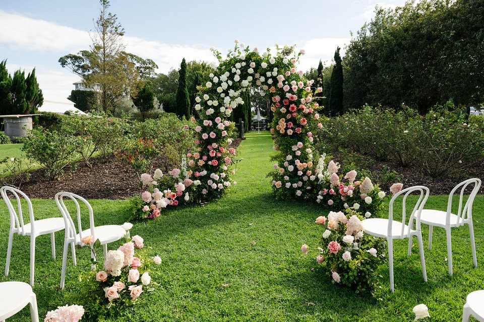 Floral arch made of pink, peach, and white roses set up for a wedding ceremony in the rose garden at The Merribee, Numbaa NSW.